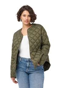 Giacca imbottita verde oliva con bottoni a pressione, collo rotondo e tessuto morbido. Indossata sopra una maglietta bianca e abbinata a jeans denim azzurri.