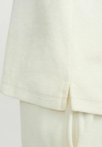 Pullover crema chiaro in tessuto morbido e testurizzato. Presenta una spaccatura laterale all'orlo e dettagli di cucitura sottile. Design semplice e rilassato.