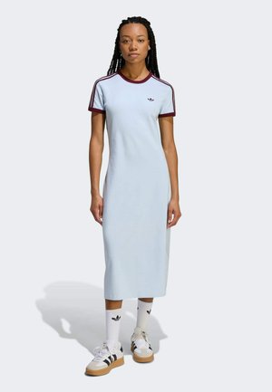 Lichtblauwe katoenen jurk met een ontspannen pasvorm, korte bordeauxrode mouwen en drie witte strepen. Model draagt witte sneakers en sokken met logo's.