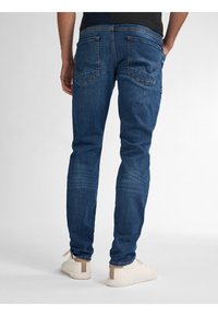 Mörkblå denimjeans med smal passform, utrustade med två bakfickor och lätt blekning på överlåren. Kombinerade med vita sneakers.