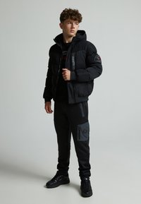 Veste doudoune noire avec fermeture éclair et capuche, dotée d'accents de logo et d'une finition texturée, assortie de joggers à panneaux noirs et gris.