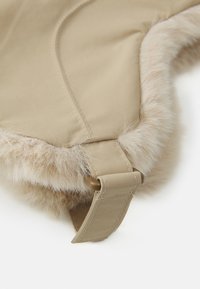 Materiale esterno beige chiaro con rifinitura in morbido pelliccia sintetica beige, dotato di una cinghia e fibbia per la chiusura. Texture liscia e dettagli di cuciture lineari.