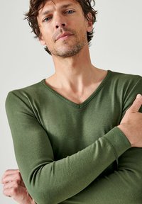 Groene longsleeve V-hals shirt met een zachte textuur, getailleerd ontwerp en eenvoudige stiksels bij de halslijn en manchetten.