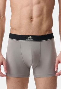 Sive raztegljive bokserice s črnim pasom, na katerem je logo Adidas, in ravnimi šivi za udobje. Gladek, oprijet dizajn.