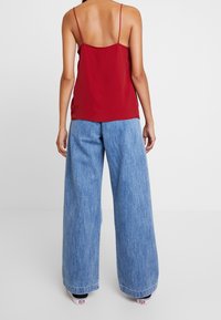 Top rosso senza maniche con spalline sottili abbinato a jeans a gamba larga blu chiaro, caratterizzati da una morbida trama in denim e da una vestibilità casual.