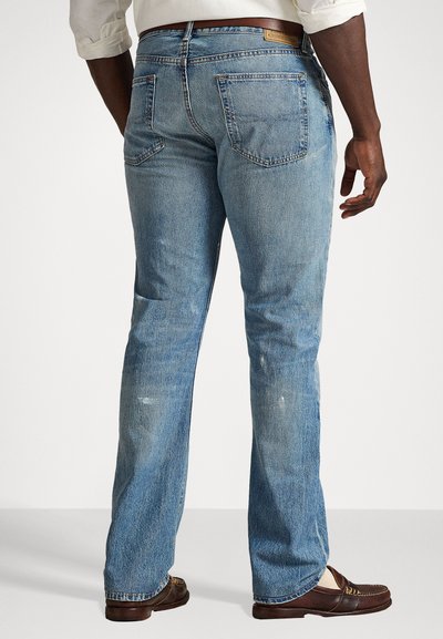 Jasnoniebieskie dżinsy dzwony z widocznymi detalami szwów, tylnymi kieszeniami, lekkimi śladami użytkowania, noszone z brązowymi loafersami.