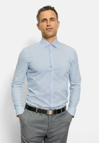 Helles blaues Langarmhemd mit einem subtilen Streifenmuster, Button-down-Kragen und Knopfverschlüssen. Getragen mit grauen maßgeschneiderten Hosen.