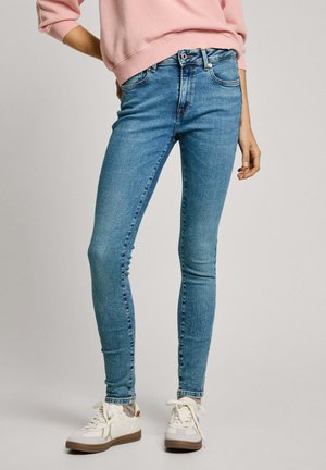 Jeans ajustados de un azul claro, hechos de denim, con un diseño clásico de cinco bolsillos y un ligero desgastado, combinados con zapatillas blancas.