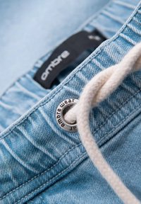 Shorts en jean bleu clair avec un cordon de serrage réglable en crème, œillet en métal argenté et étiquette noire avec le logo "ombre".
