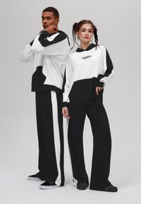 Sweatshirts en noir et blanc avec de larges blocs de couleur, associés à des pantalons à jambes larges avec des rayures. Texture de tissu lisse, design décontracté.