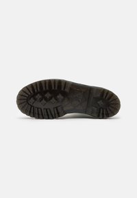 Semelle d'une botte noire robuste avec des crampons profonds et à motifs, conçue pour assurer une bonne traction sur différentes surfaces.