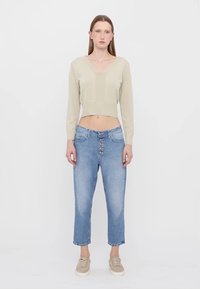 Maglione cropped beige chiaro con orlo a coste, abbinato a jeans blu chiaro a vita alta con chiusura a bottoni e gambe dritte. Scarpe chiare.