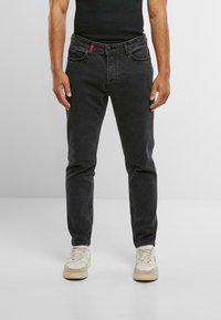 Vaqueros de mezclilla negra de corte slim, con bolsillos estándar y un acento rojo en la parte frontal. Combinados con zapatillas de color claro.
