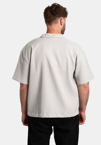 Camicetta grigia a maniche corte con una sottile texture a coste, vestibilità ampia e orlo arrotondato, con un colletto semplice e senza componenti metallici visibili.