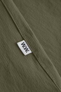 Olívová látka s textúrovaným tkaním, s bielou nášivkou "W.W." pri okraji.