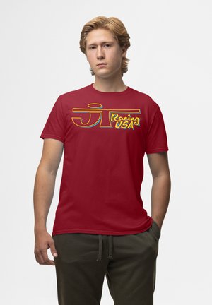 Rød bomulds-T-shirt med korte ærmer, der har et gult og blåt "JT Racing USA" logo grafisk motiv på forsiden. Enkel design og rund halsudskæring.