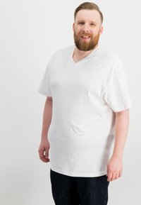 Weißes V-Ausschnitt-T-Shirt aus weicher Baumwolle, mit kurzen Ärmeln und lässigem Schnitt, kombiniert mit dunkler Jeans.