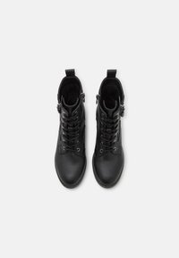 Botas de cuero negro hasta el tobillo con cordones en la parte frontal, puntera redonda y cremallera lateral. Presenta una superficie texturizada y una lengüeta para facilitar su uso.