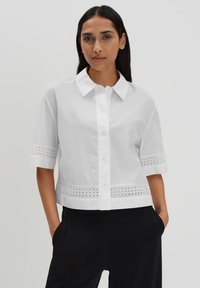 White short-sleeve shirt with a button front, featuring eyelet details along the hem. Made from lightweight fabric, offering a relaxed fit.