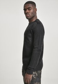 Jersey de punto negro con un cuerpo texturizado, acentos de cuero en los hombros y un bolsillo delantero. Los puños y el dobladillo acanalados completan el diseño.