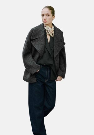 Manteau en laine gris avec des revers surdimensionnés, associé à un haut noir et un pantalon en denim foncé ample ; présente une écharpe légère à motifs autour du cou.