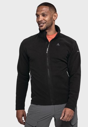 Black fleece jacket with a stand-up collar, front zipper, side pockets, and a logo on the chest. Worn over an orange shirt.