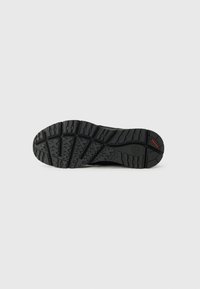 Schwarze Schuhsohle mit einem robusten Profil, das ausgeprägte erhöhte Abschnitte aufweist und ein rotes Akzent nahe der Ferse zur Verbesserung des Grips hat.