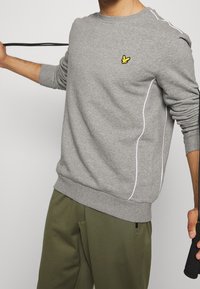 Gray sweatshirt made of soft fabric, features a ribbed crew neck, white side piping, and a small yellow bird logo on the chest.