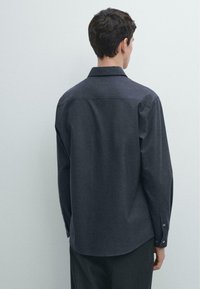 Donkergrijs shirt met lange mouwen, gemaakt van textuurstof. Voorzien van een button-down kraag, manchetten met knopen en een licht gebogen zoom.