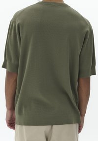 Zelený pletený svetr s krátkým rukávem, kulatým výstřihem, strukturovanou tkaninou a volným střihem. Spodní okraj je mírně zúžený s bočními rozparky.