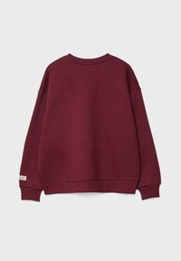 Bordeaux crewneck sweatshirt med ribbet ærmer og kant, med et lille hvidt "University of Cambridge" label på venstre ærmekant.