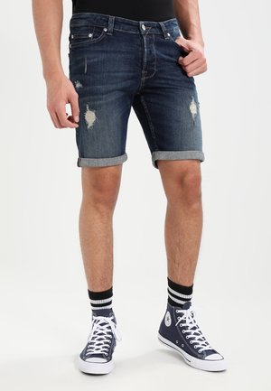 Donkerblauwe denim shorts met versleten details, opgerolde boorden en een vijf-pocket ontwerp. Gecombineerd met marineblauwe high-top sneakers en gestreepte sokken.