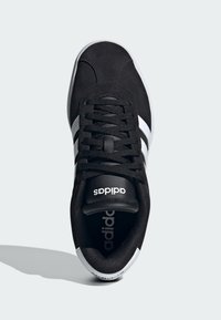 Czarny sportowy but z białym trójpaskowym wzorem, górna część z teksturowanego materiału, sznurówki i oznaczenie marki na języku. Gumowa podeszwa widoczna przy pięcie.
