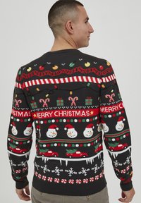 Svart julesweater med fargerike snømenn, sukkertøy, gaver og festlige mønstre. Strikket stoff med rillede mansjetter og nederkant.