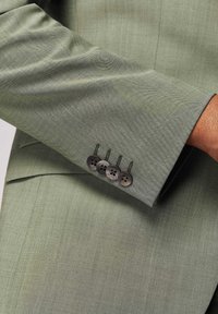 Jasnozielona marynarka w stylu dopasowanym, charakteryzująca się gładką fakturą, wyraźnym klapą i czterema ciemnymi guzikami na mankietach.