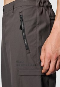 Grå byxor med en dragkedjeficka, texturerad tyg, elastisk midja och tryckt text som säger "HALO 196819721981" på benet.