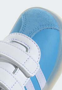 Baskets bleues avec des textures en cuir et en suède, des bandes Velcro blanches et des détails de couture distinctifs. Bout arrondi avec semelle en caoutchouc.