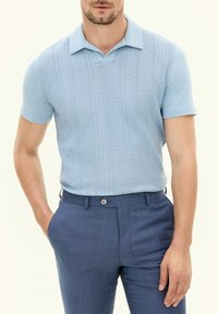Polo bleu clair à manches courtes avec un motif textur�é et un col classique, associé à un pantalon tailleur bleu foncé avec un bouton.