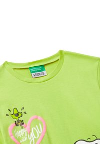 Limetkově zelené tričko s textem "Šťastný s tebou", růžovým srdcem a kresleným ptáčkem z Peanuts blízko štítku na límci.