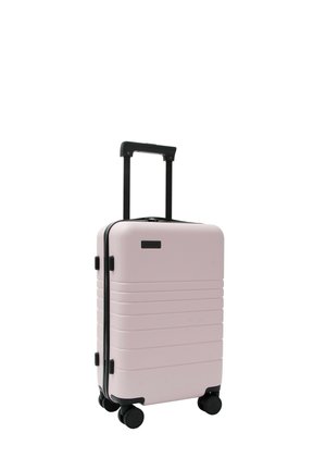 Valise rigide rose avec quatre roues noires et une poignée télescopique noire étendue sur fond blanc.