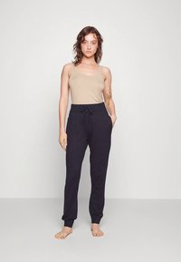 Bézs ujjatlan felső sötétkék jogger nadrággal párosítva. A nadrág húzózsinóros derékrésszel és mandzsettás bokával rendelkezik, puha anyagból készült.