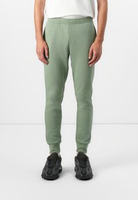 Lys grønne joggere lavet af blødt stof, med elastisk talje og tætsiddende mansjetter, parret med sorte sneakers.
