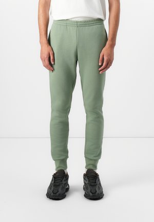 Lichtgroene joggers van zachte stof, met een elastische tailleband en nauwsluitende boorden, gecombineerd met zwarte sneakers.