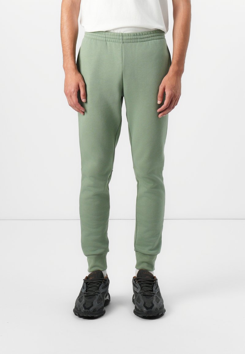 Lys grønne joggere lavet af blødt stof, med elastisk talje og tætsiddende mansjetter, parret med sorte sneakers.