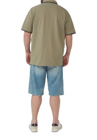 Khaki poloshirt met zwarte afwerking, gecombineerd met lichtblauwe denim shorts. Model met witte schoenen met donkere accenten, gezien vanuit de achterkant.