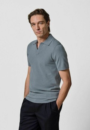 Polo a maniche corte in azzurro chiaro, realizzata in tessuto texturizzato. Presenta un colletto classico e una vestibilità comoda. Indossata con pantaloni scuri.