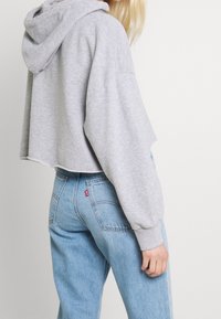 Felpa grigia tagliata in tessuto morbido con maniche lunghe, dotata di cappuccio regolabile e polsini a coste, abbinata a jeans azzurri a vita alta.