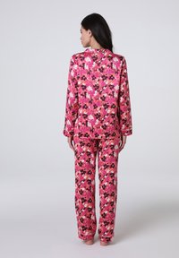 Set di pigiama floreale rosa composto da una maglietta a maniche lunghe e pantaloni. Tessuto morbido con un vivace motivo di fiori in tonalità di rosa, bianco e marrone.