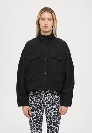 Black cropped jacket made of lightweight material, featuring a high collar, dual chest pockets, and button closures. Worn over leopard print pants.
