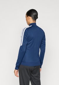 Μπλε ναυτικό αθλητικό μπουφάν με μακριά μανίκια, λευκές ρίγες στα πλευρά, ψηλό γιακά και εφαρμοστή γραμμή. Ομαλή υφή με ριμπ μανσέτες.